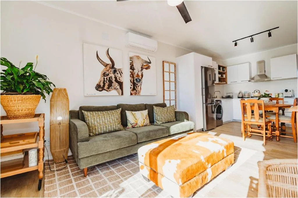 Modern lounge with gray sofa, orange ottoman, and open-plan kitchen visible