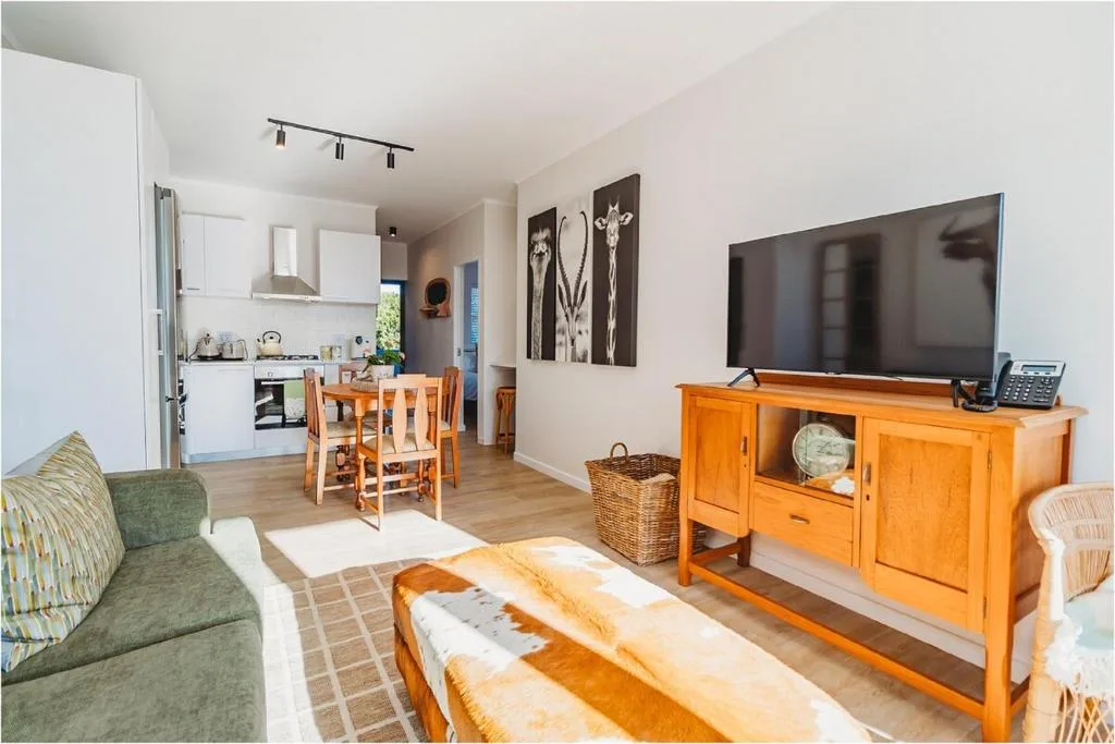 Open-plan lounge with green sofa, wooden TV unit, and kitchen view