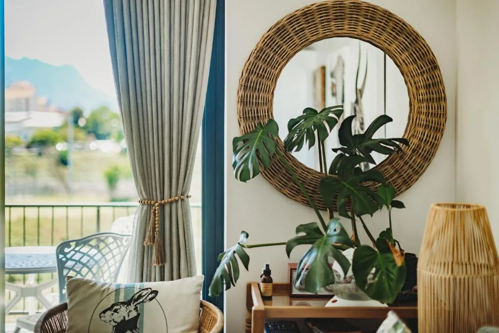Stylish lounge with woven mirror, potted plants, and mountain views through windows