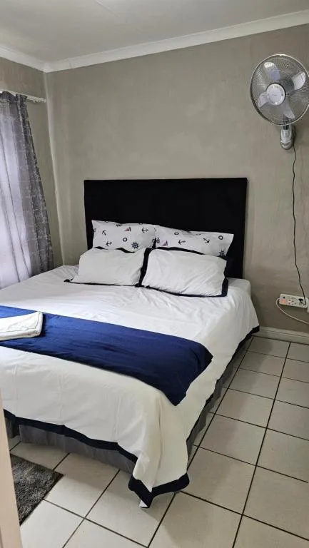 Bedroom with black headboard, white bedding, blue throw, and standing fan