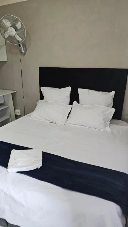 Bedroom with black headboard, white linens, and standing fan