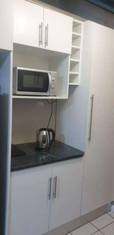 Modern kitchenette with microwave, kettle, and black countertop storage