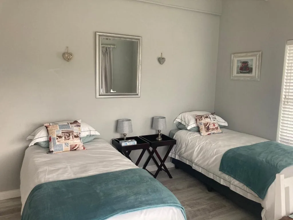 Twin bedroom with two beds, teal blankets, shared nightstand, and mirror