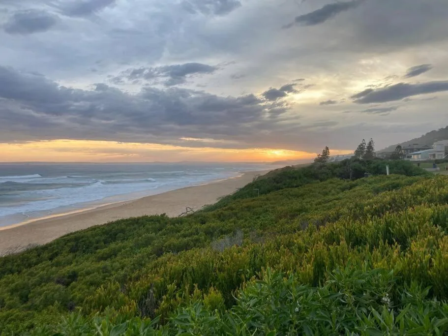 Sunset over beach with coastal dunes and property nestled on hillside