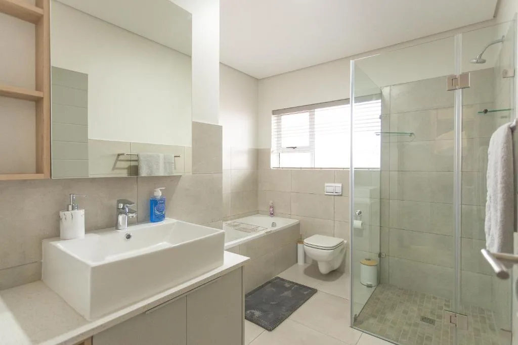 Modern bathroom with double vanity, glass shower enclosure, and toilet
