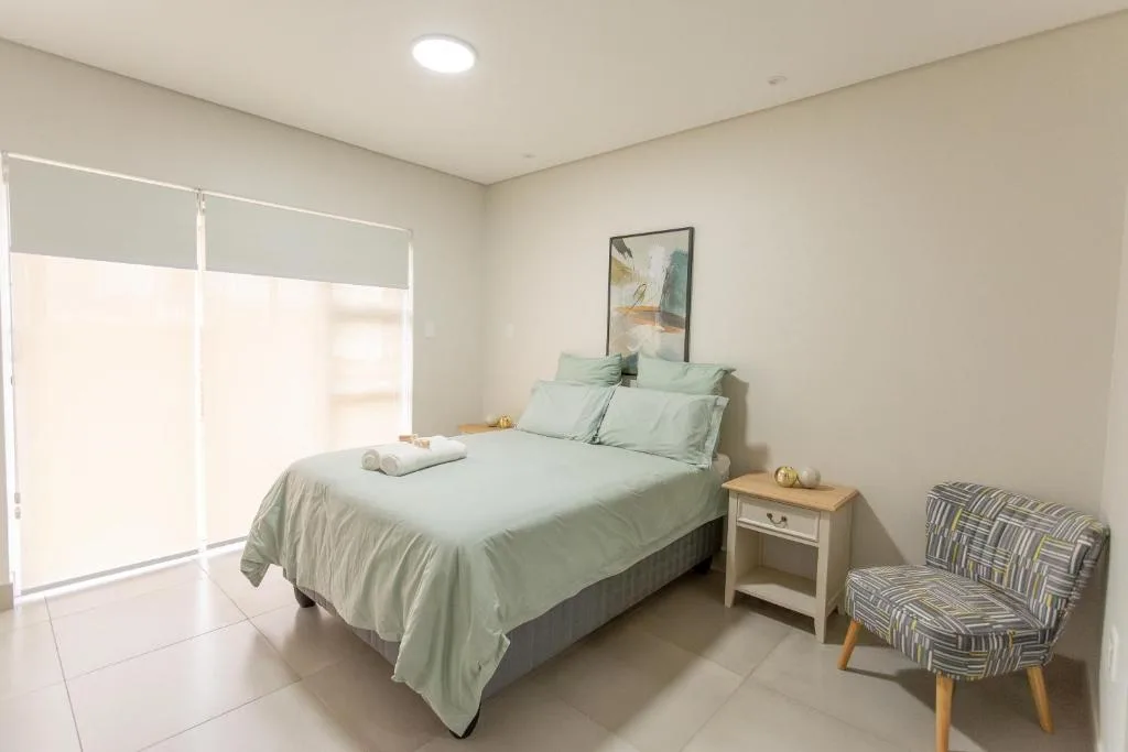 Bright bedroom with sage green bedding, wooden nightstand, and striped accent chair