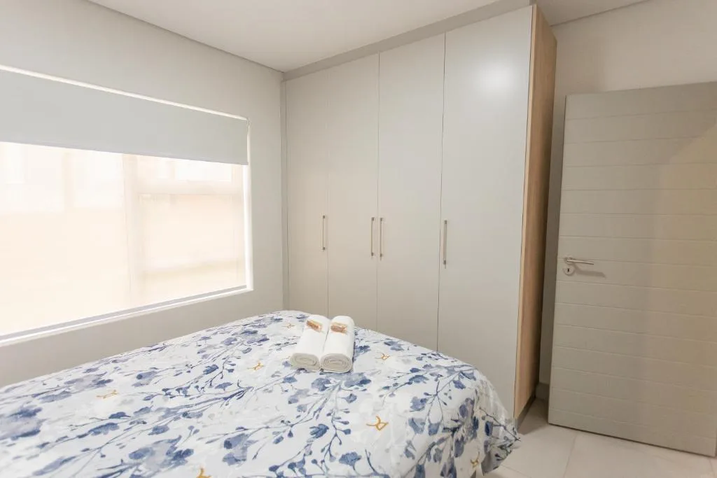 Modern bedroom with queen bed, white built-in wardrobes, and bright window