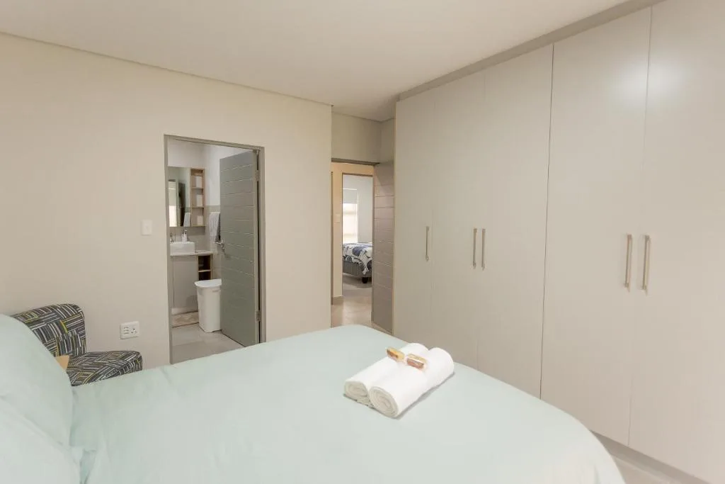 Modern bedroom with white bedding, en-suite bathroom, and built-in wardrobes