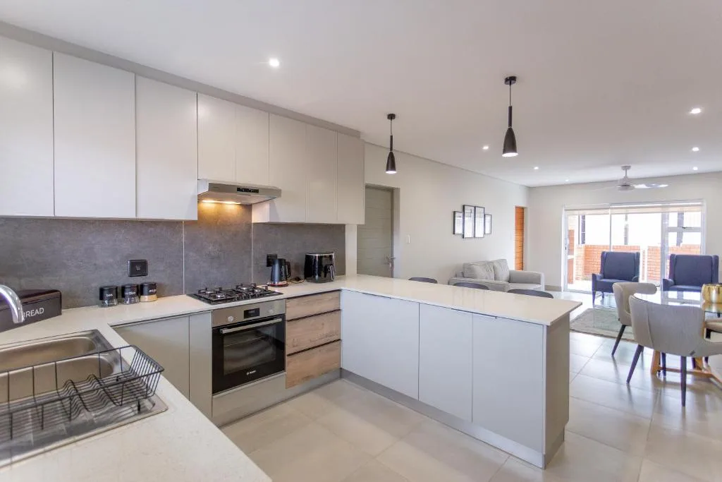 Modern white kitchen with island, gas stove, and open plan lounge beyond