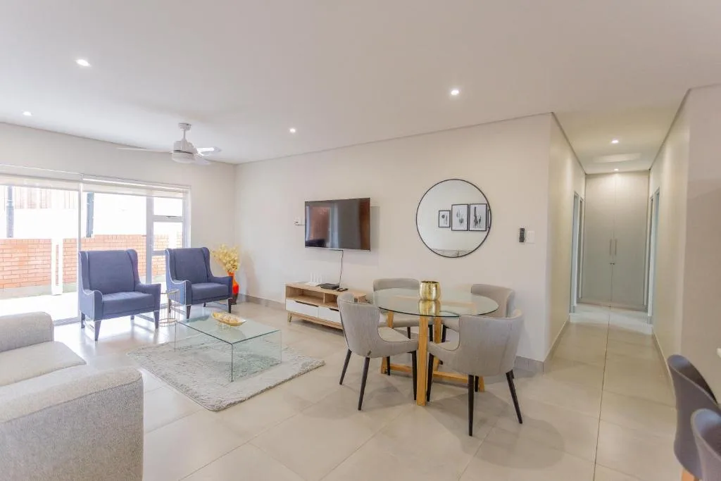 Modern open-plan lounge with dining area, blue armchairs, and wall-mounted TV