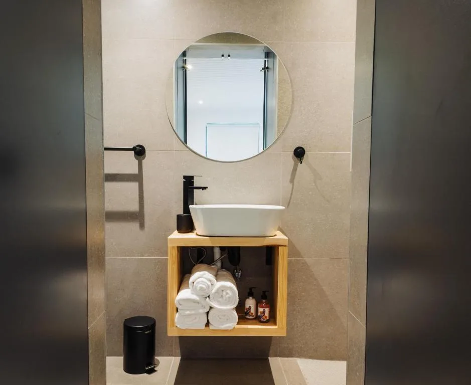 Modern bathroom vanity with round mirror, white vessel sink, and towel storage