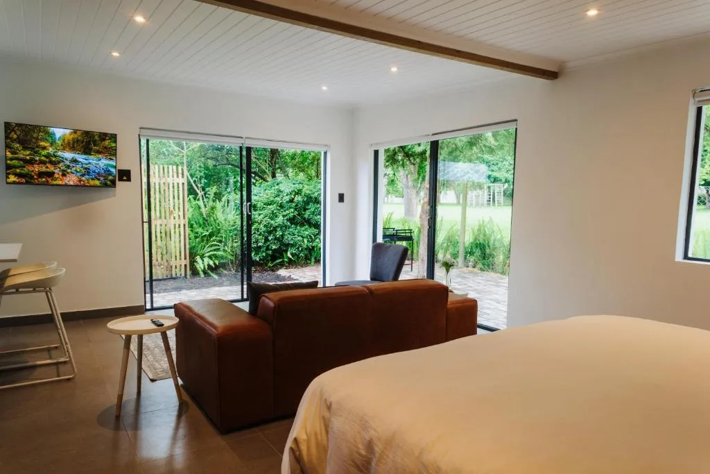 Modern bedroom with bed, brown sofa, and garden views through glass doors
