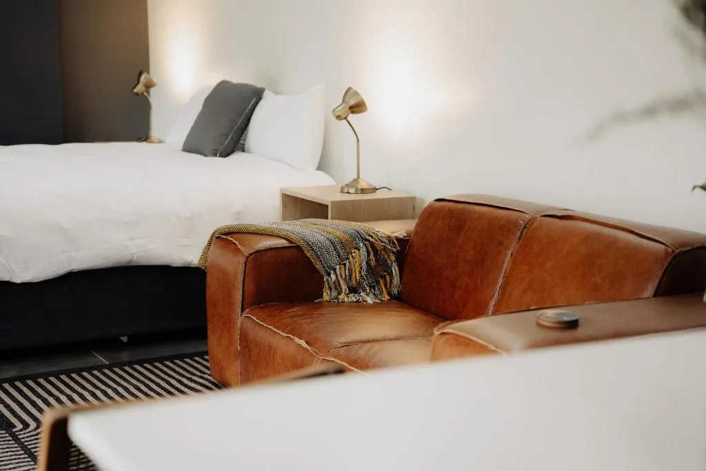 Modern bedroom with white linens, cognac leather sofa, and brass reading lamp