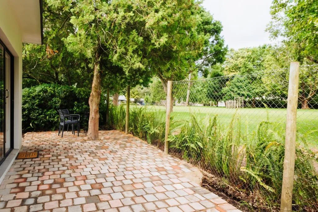 Brick paved patio with seating beneath mature trees and fenced garden