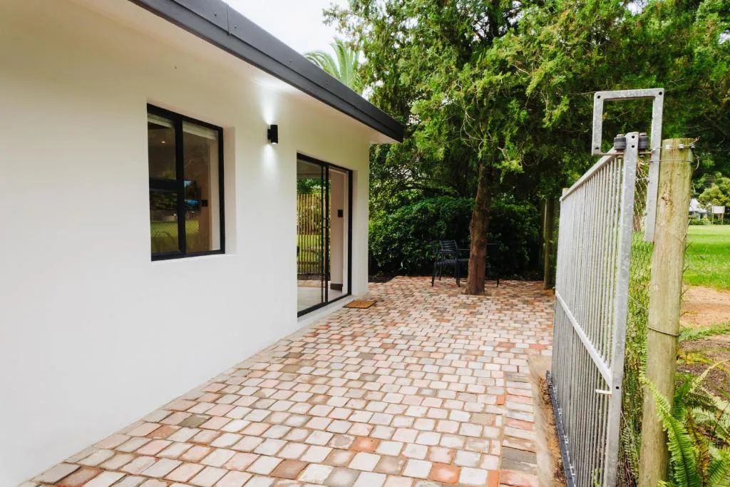 Paved patio area with modern white cottage and lush garden surroundings