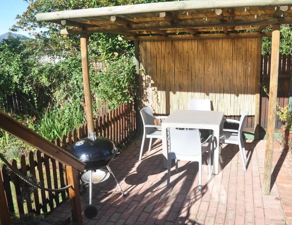 Wooden pergola deck with dining table, chairs, and braai grill