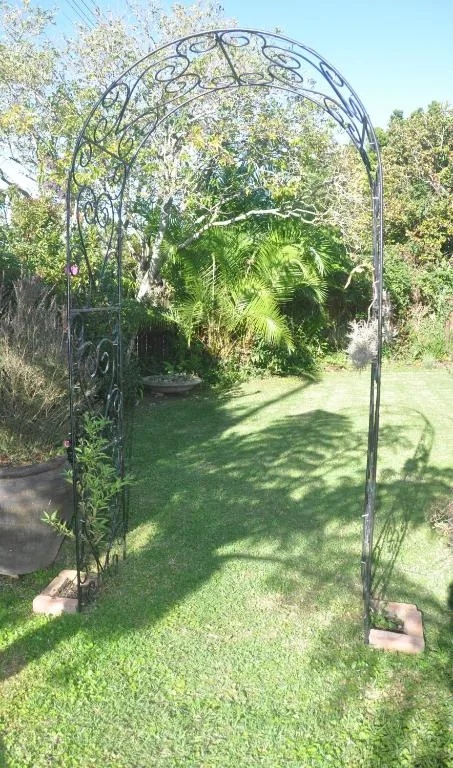 Ornate wrought iron garden arch framing lush green lawn and tropical plants
