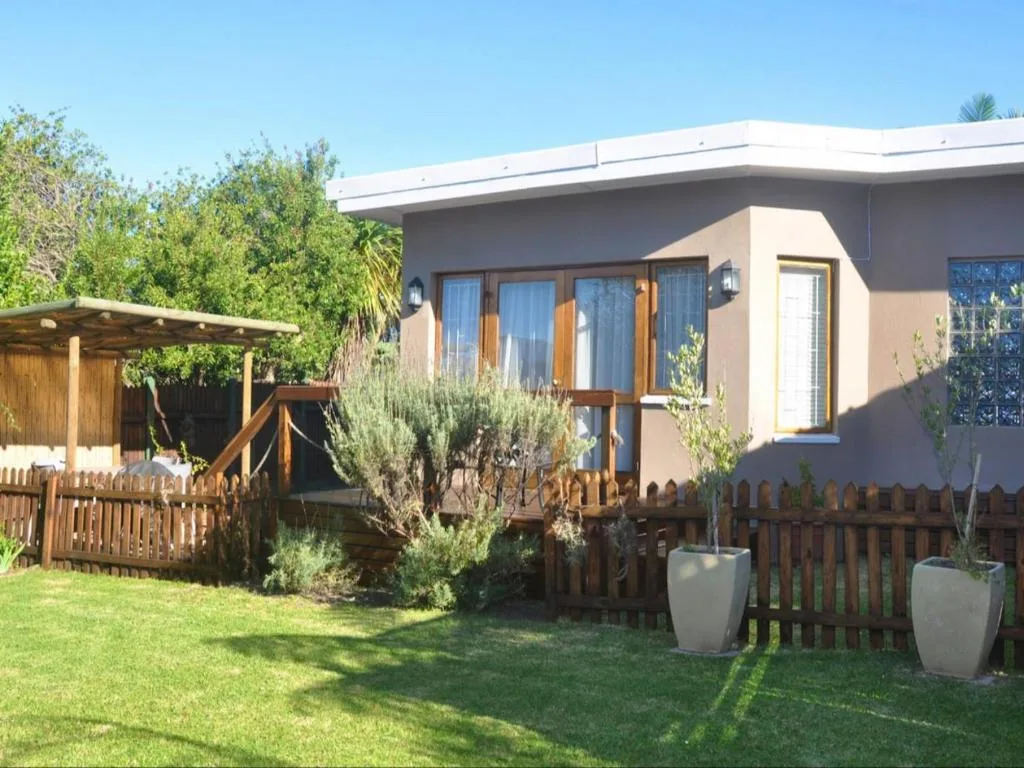 Modern beige cottage with wooden deck, landscaped garden, and fencing