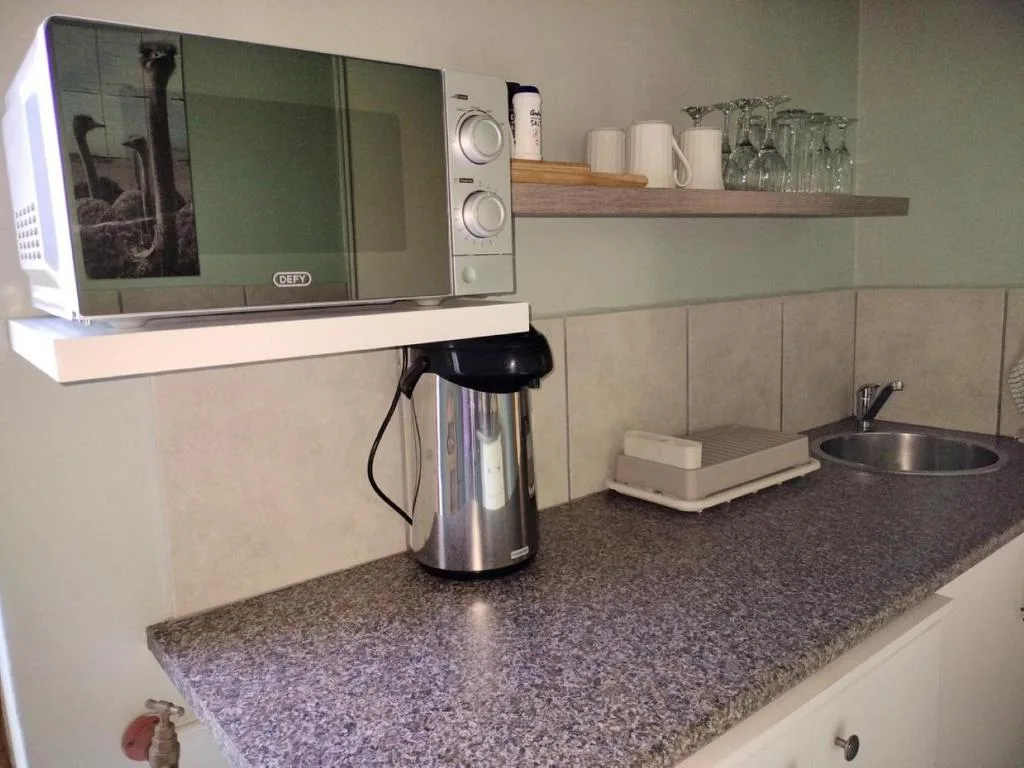Modern kitchen with microwave, kettle, countertop and wooden shelf with glassware