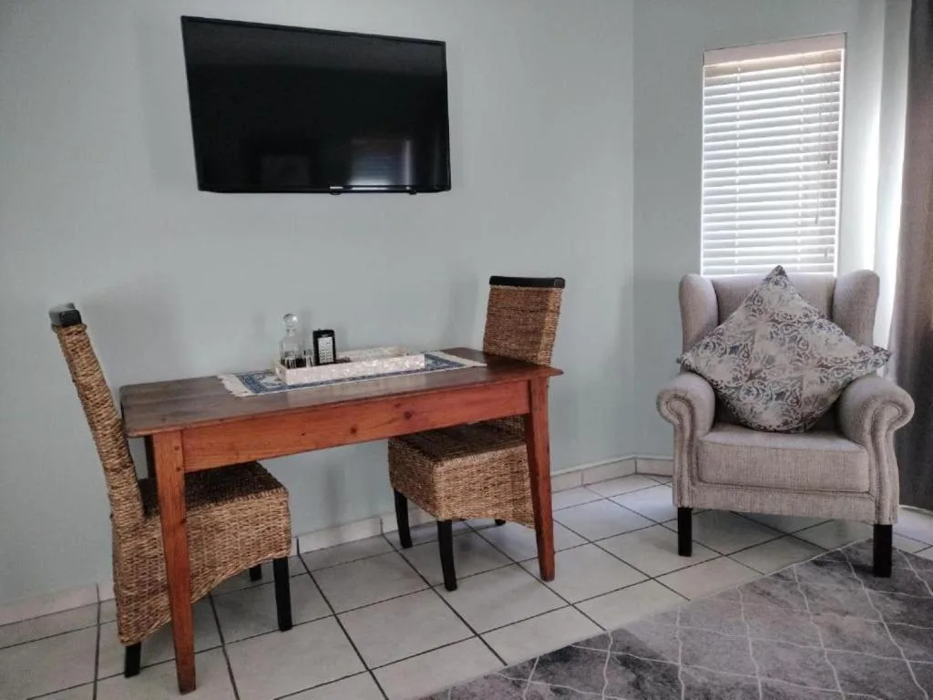 Living room with TV, comfortable armchair, wooden desk, and natural light from shuttered windows
