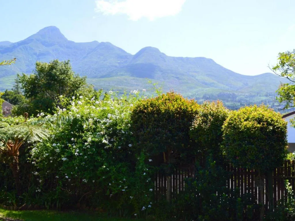 Majestic mountain peaks rise beyond lush garden with flowering shrubs