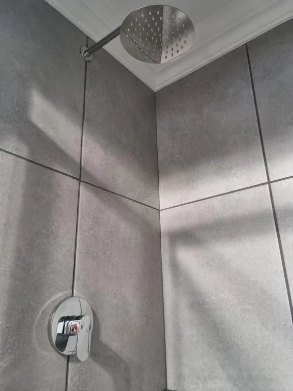 Modern shower with rainfall showerhead and chrome fixtures in tiled bathroom