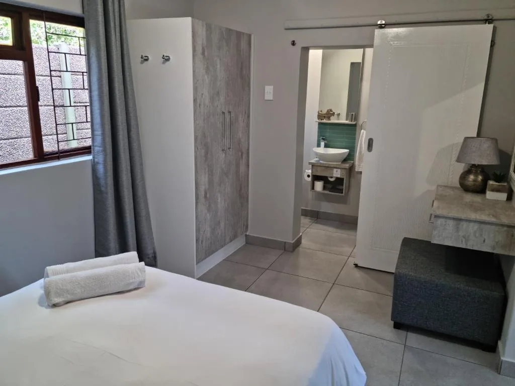 Bright bedroom with white bed, ensuite bathroom visible through open door