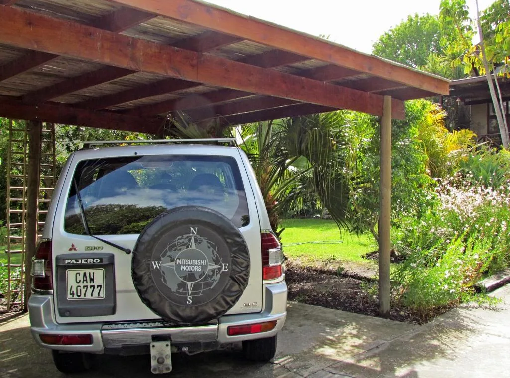 White Mitsubishi Pajero parked under wooden carport with lush garden surroundings