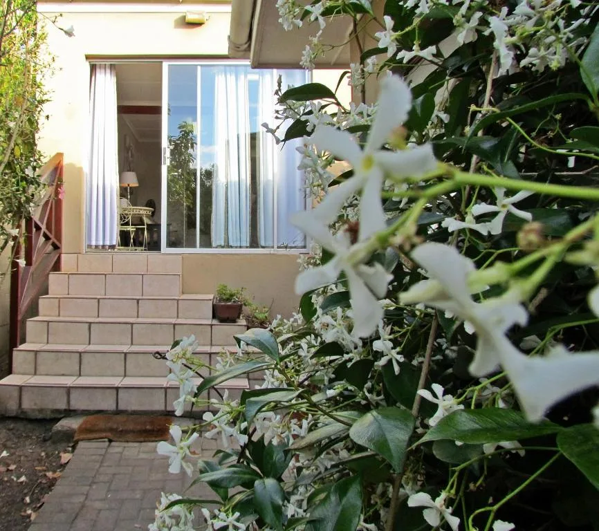 White flowering jasmine vines frame the entrance steps and glass doors of the cottage