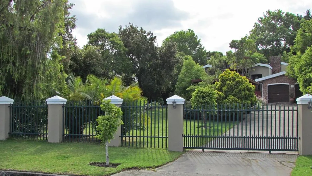 Brick home behind black metal gates with manicured gardens and mature trees
