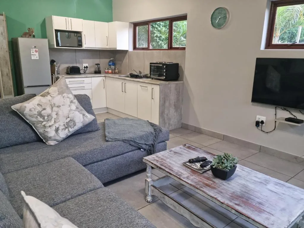 Open-plan lounge with grey sofa, TV, and integrated kitchen area visible