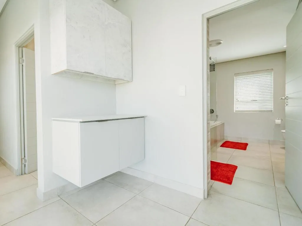 Modern white bathroom with vanity, shower enclosure, and red bath mats