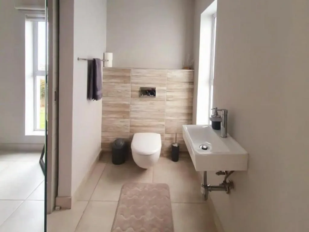 Modern bathroom with toilet, wall-mounted sink, and wood-tile accent wall