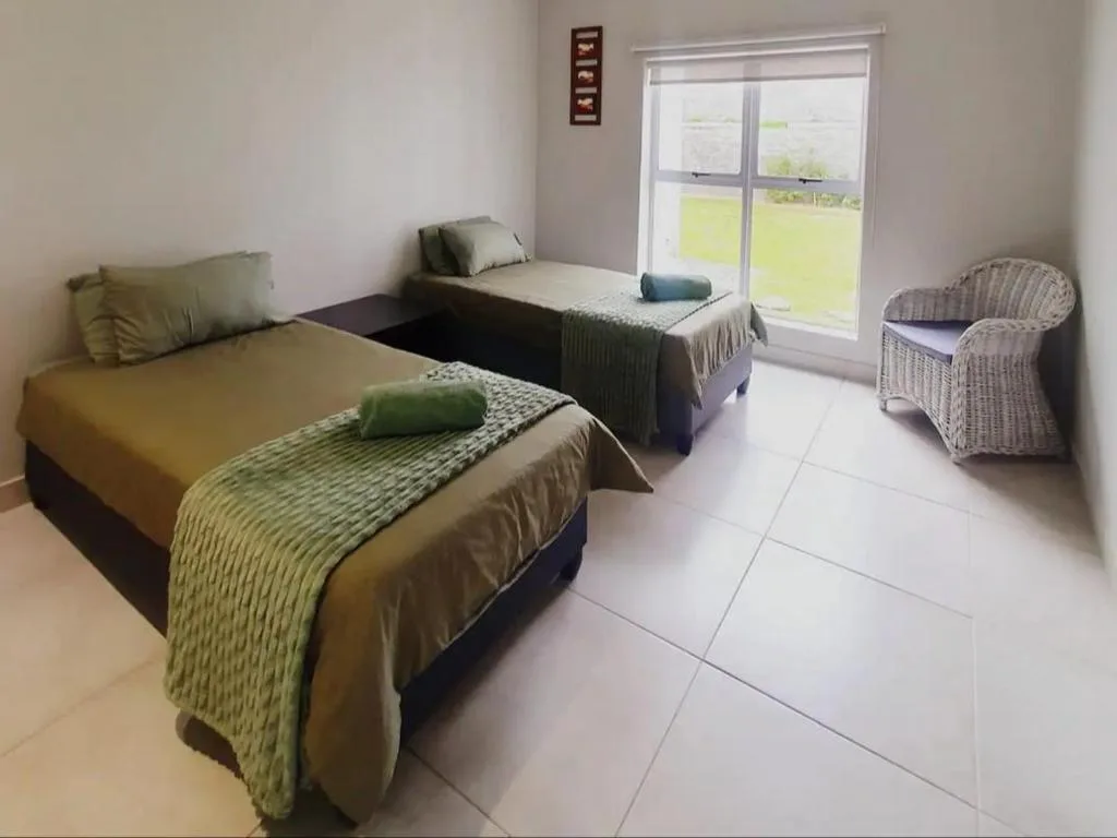Twin bedroom with olive bedding, wicker chair, and garden views