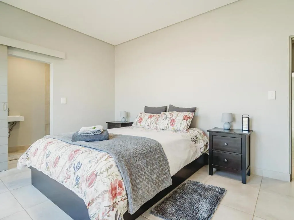 Bright bedroom with queen bed, floral bedding, dark nightstands, and ensuite bathroom