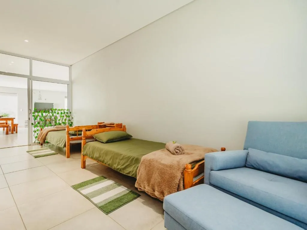 Bright bedroom with two wooden-frame beds and green bedding, blue sofa visible