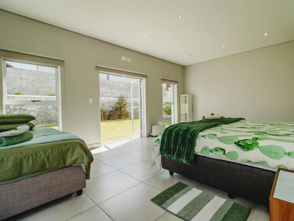 Bright bedroom with two beds, green bedding, and garden views through sliding doors