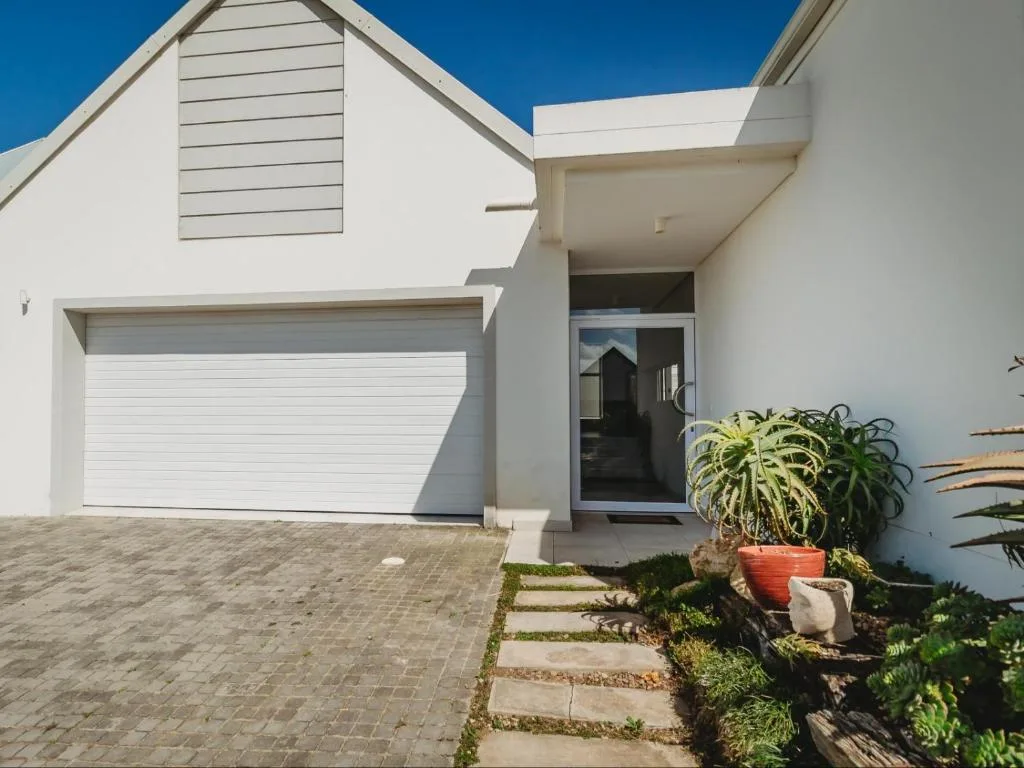 Modern white home with garage, entrance, and landscaped garden beds