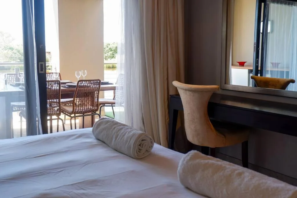 Spacious bedroom with white bedding, desk, and views to dining area beyond