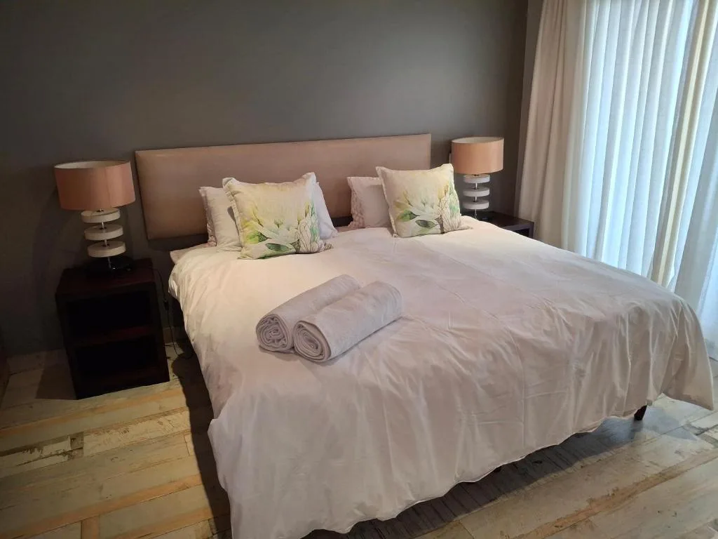 Modern bedroom with queen bed, floral pillows, rolled towels, and bedside lamps