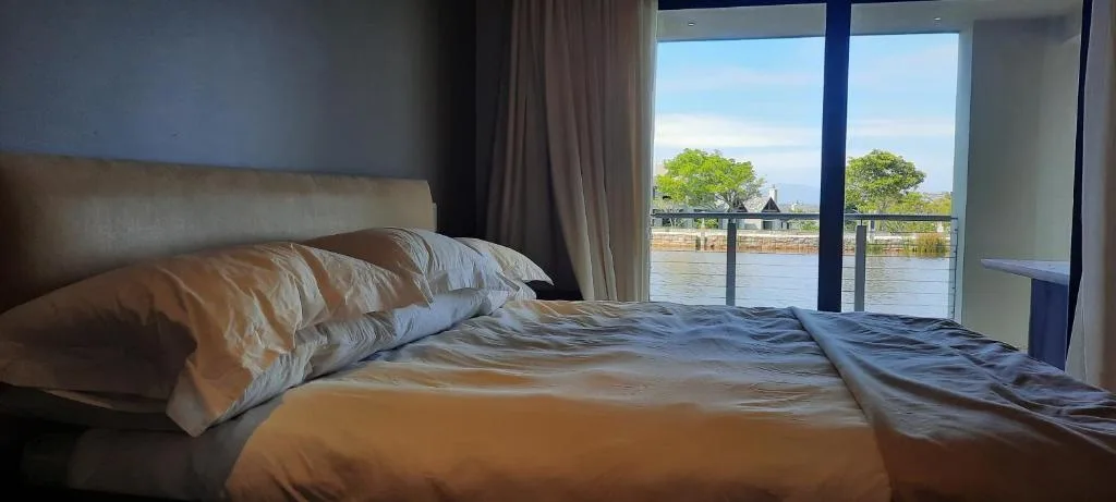 Spacious bedroom with bed overlooking lagoon and trees through large windows