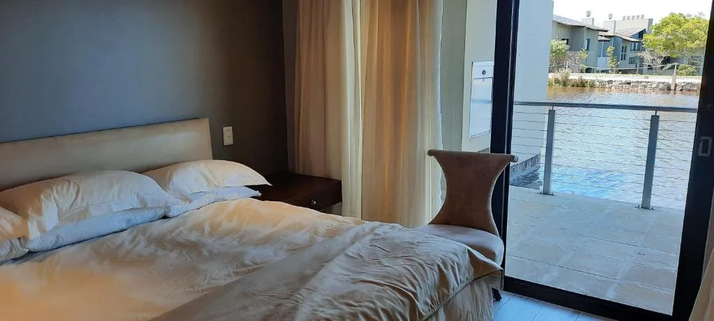 Modern bedroom with waterfront view through glass doors and deck access