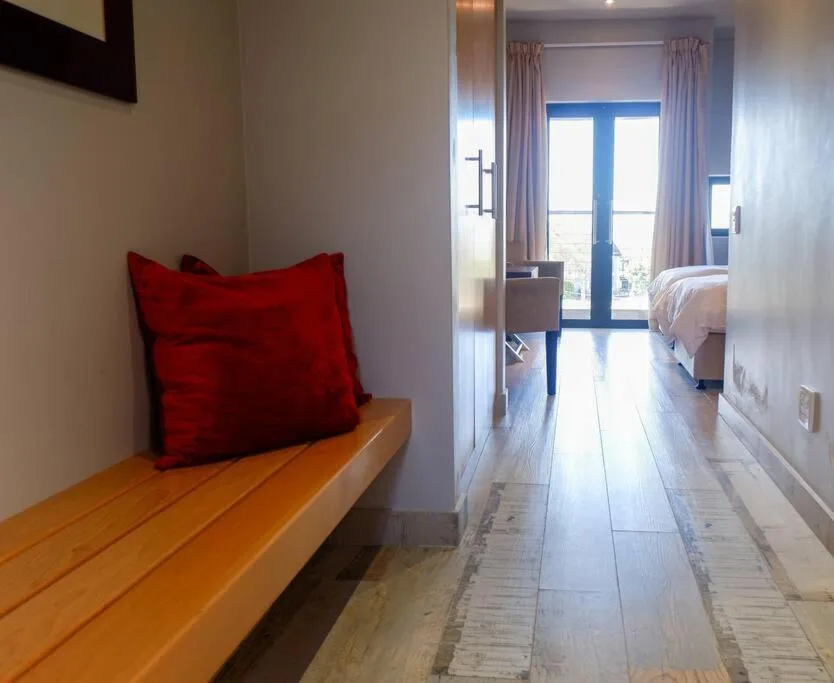 Bright bedroom with red cushion on wooden bench and glass doors
