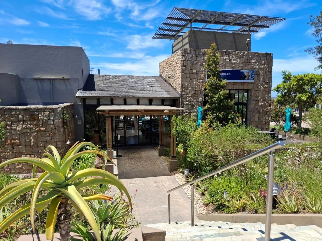 Modern stone building entrance with pergola and manicured garden landscaping