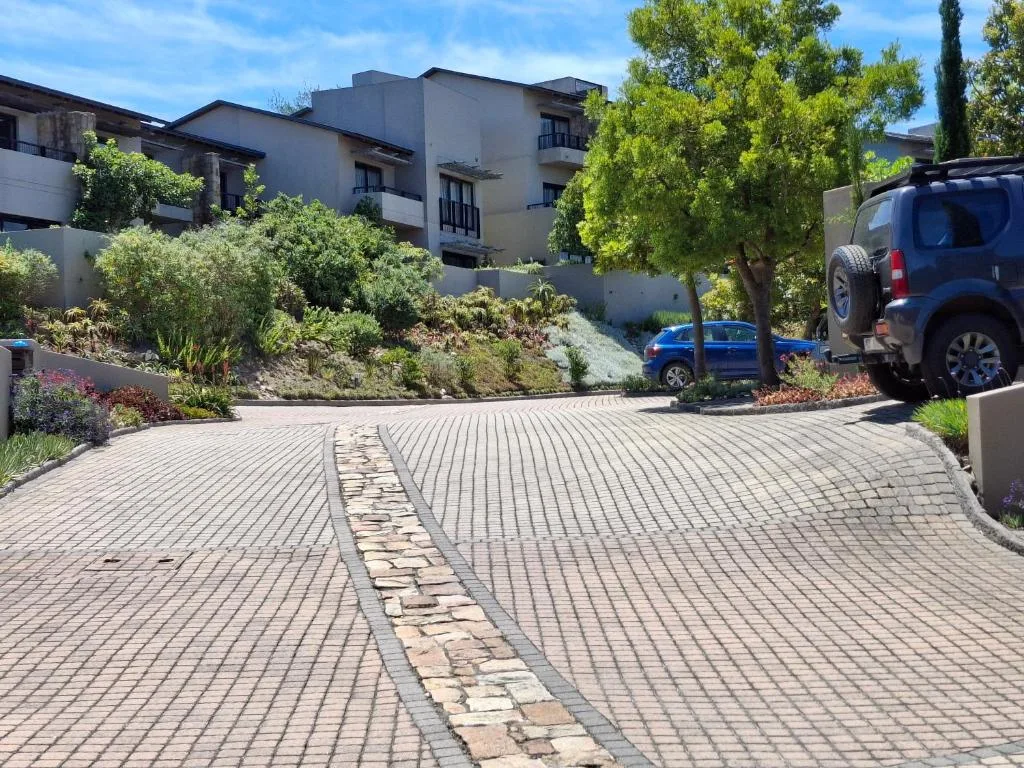 Modern apartment building with manicured gardens, paved driveway, and parked vehicles