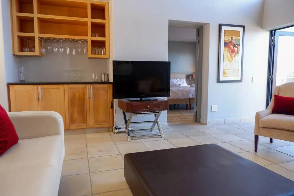 Open-plan lounge with TV, cream sofa, wooden cabinetry, and glass doors to patio