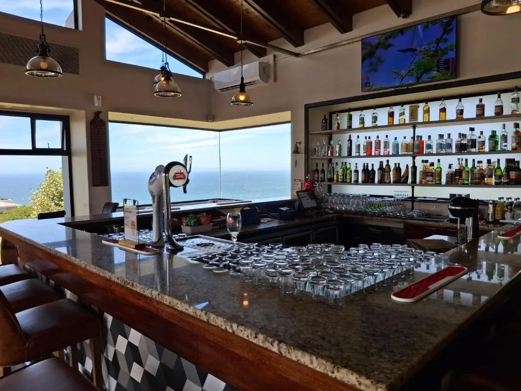 Modern bar area with ocean view, spirits bottles, and coastal landscape visible through windows