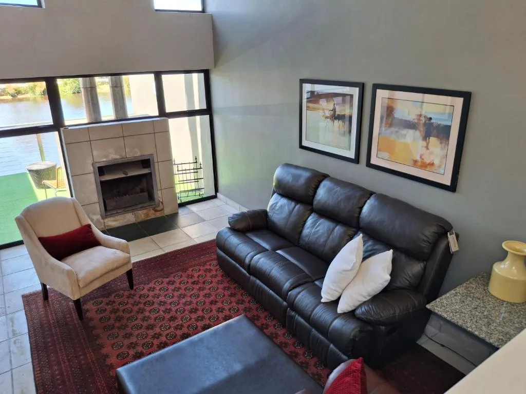 Modern lounge with black leather sofa, fireplace, and waterfront views