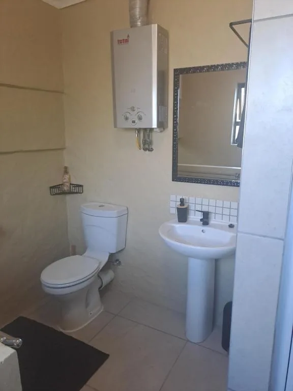 Compact bathroom with toilet, pedestal sink, mirror, and wall-mounted water heater