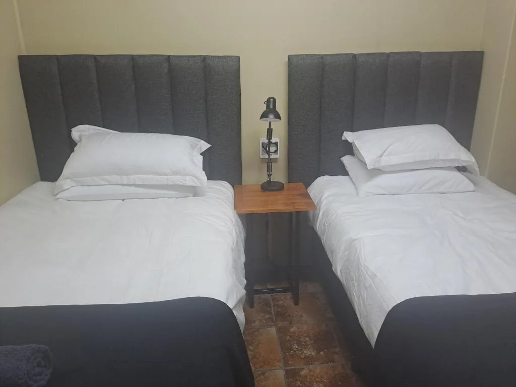 Twin bedroom with white linens, grey upholstered headboards, wooden bedside table